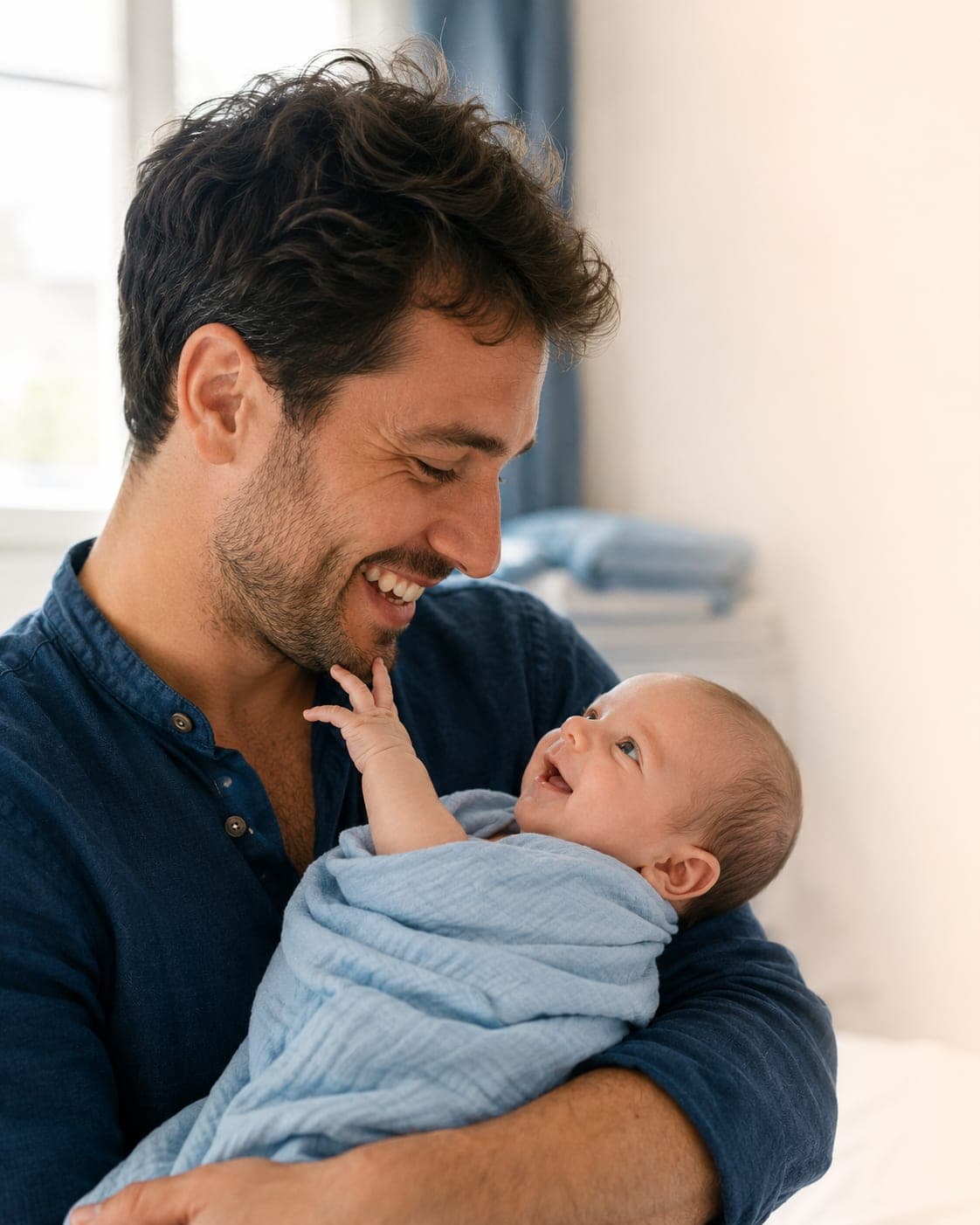 Un jeune père souriant tenant son nouveau-né enroulé dans un lange bleu